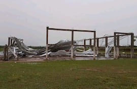 Estructura metálica en ruinas en un terreno cubierto de hierba, bajo un cielo nublado.
