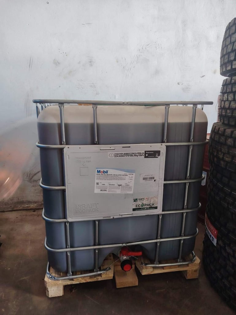 Contenedor de plástico etiquetado con 'Mobil', rodeado de neumáticos en un ambiente industrial interior.