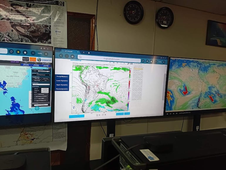 Centro de monitoreo con tres pantallas mostrando mapas meteorológicos y datos sobre precipitación, sin personas visibles.