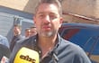 Pedro Alliana con camisa oscura sostiene un micrófono mientras un grupo de hombres lo observa en el fondo, ambiente exterior con pared de ladrillos.