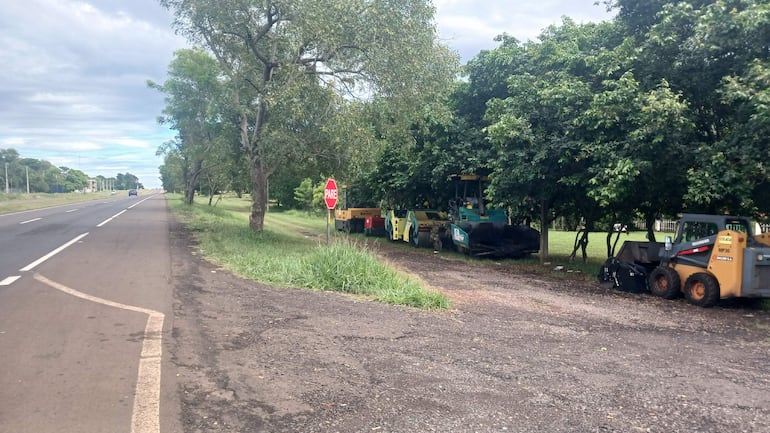 Carretera con pavimento en asfalto. A la derecha, maquinaria pesada y vehículos de construcción. Señal de tránsito 'PARE' visible.