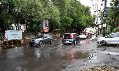 Calle Gral Santos con tráfico, charcos de agua, un automóvil gris y un SUV azul entre otros coches, bajo un cielo nublado.