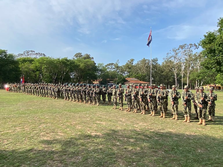 Formación de 40 soldados en camuflaje, con cascos y armas, bajo bandera paraguaya y roja en un ambiente solemne.