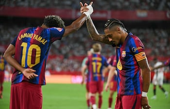 El delantero brasileño del Barcelona, Raphinha celebra con el delantero español Lamine Yamal, tras marcar el segundo gol de su equipo durante el partido de fútbol de la liga española, en el estadio Ramón Sánchez Pizjuán.