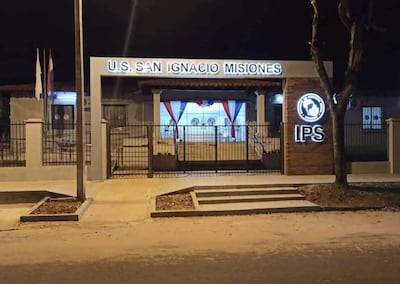 Sede del IPS en San Ignacio, iluminada de noche, con banderas y adornos en la entrada.