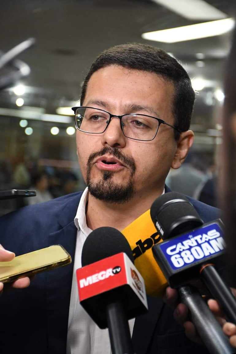 Miguel Sosa con chaqueta oscura y camisa clara, rodeado de periodistas con micrófonos en conferencia de prensa.