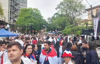 Multitud vestida de blanco y con banderas de Paraguay, enérgica en protesta, escuchando a un orador en una plataforma sobre un vehículo.