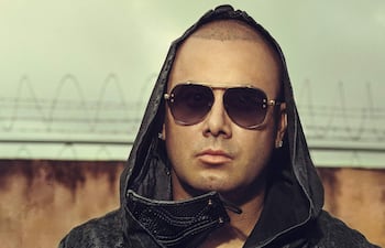 Wisin lleva gafas de sol y un abrigo elegante, posando con una actitud tranquila en el evento.