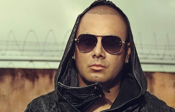 Wisin lleva gafas de sol y un abrigo elegante, posando con una actitud tranquila en el evento.
