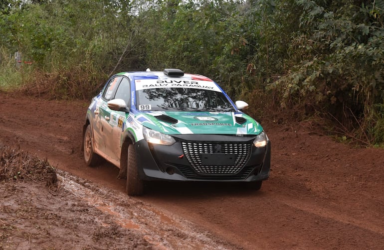 Automóvil Peugeot número 99 en colores verde y azul, recorriendo un camino de tierra en un entorno forestal.