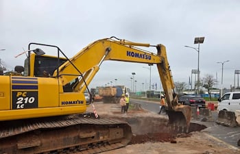 Excavadora Komatsu amarilla en la vía pública, rodeada de trabajadores con cascos y ropa de trabajo, en medio de una obra.