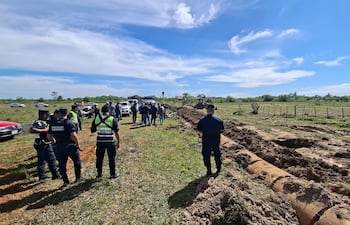 Siete agentes de la Policía Nacional, en uniforme oscuro, conversan en un terreno rural con una excavadora al fondo.