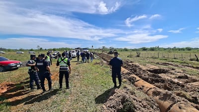 Siete agentes de la Policía Nacional, en uniforme oscuro, conversan en un terreno rural con una excavadora al fondo.