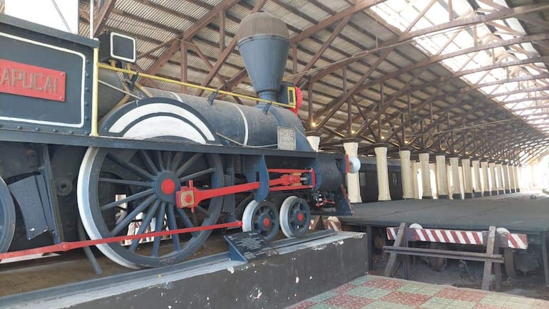 Locomotora de vapor 'APUCAI' de color negro con ruedas rojas, en un museo con estructura de vigas de madera.