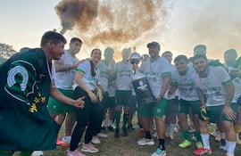 Grupo de personas sonrientes con camisetas blancas que dicen 'CAMPEONES 2023', sosteniendo un trofeo en un ambiente festivo.