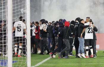 TOPSHOT - Fans of Colo Colo enter the pitch during the Copa Libertadores group stage football match between Chile's Colo Colo and Brazil's Fortaleza at the Monumental David Arellano stadium in Santiago, on April 10, 2025. Two people were killed Thursday in a stampede as a group of fans tried to force their way into Colo Colo's Monumental stadium in Santiago to watch the match against Brazil's Fortaleza for the Copa Libertadores 2025, authorities said. (Photo by Javier TORRES / AFP)