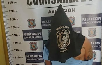 Hombre de espaldas con gorro negro y camiseta azul, frente a fondo de la Comisaría 24 de Asunción.