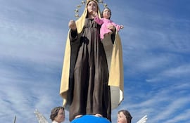 Estatua de la Virgen María rodeada de personas en oración, cielo nublado y vegetación al fondo.