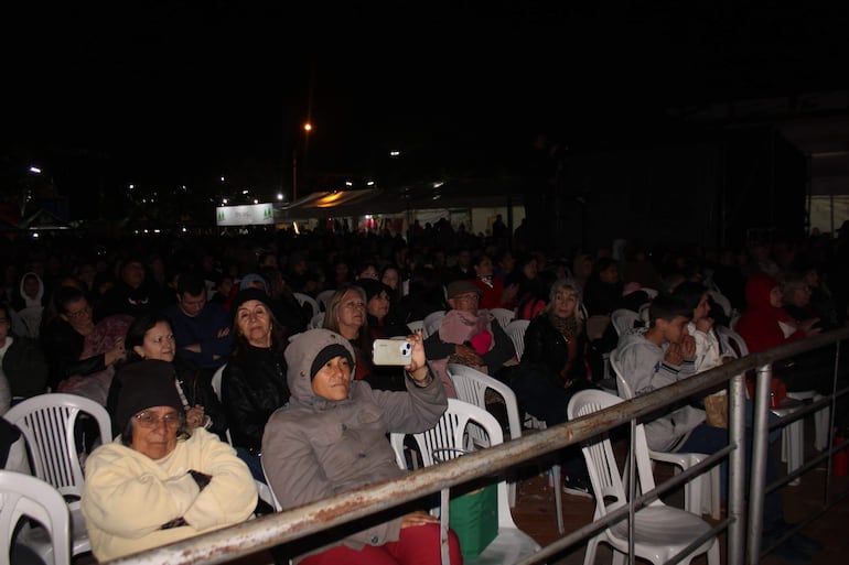 Gran multitud asiste al Festival del Lago Ypacarái, con personas sentadas en sillas blancas y una mujer grabando con su teléfono.