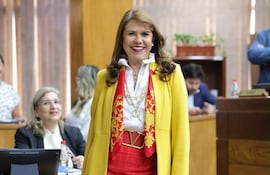 Celeste Amarilla sonríe en chaqueta amarilla y falda roja, interactuando con otra mujer en un ambiente formal.