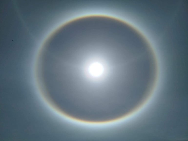El sol brilla intensamente rodeado por un círculo luminoso con colores difusos en un cielo despejado.