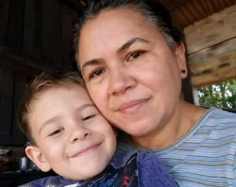 Una mujer con blusa de rayas y un niño con camiseta oscura sonríen en un ambiente acogedor con luz natural.