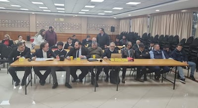Grupo de hombres de negocios y políticos en trajes formales discuten en mesa larga con micrófono, en un ambiente institucional.