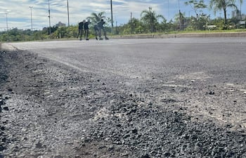 Tres patinadores en carretera, dos avanzando y uno en pausa, bajo cielo despejado y vegetación en el entorno.