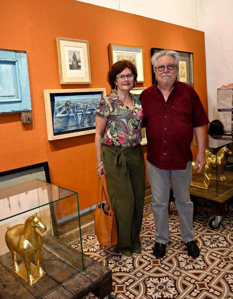 Félix Toranzos, de cabello canoso y gafas, junto a mujer sonriente con blusa colorida, observan una escultura en galería.