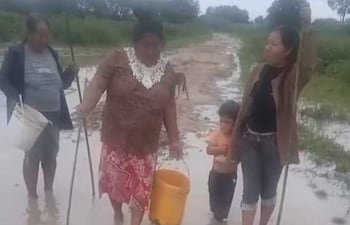 Tres mujeres y un niño en un área anegada, con una mujer sosteniendo un balde amarillo y la otra un palo. Clima nublado.