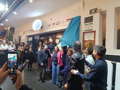 Hombre emocionado con telón azul, mujer en abrigo fucsia a su lado, asistentes sonrientes y ambiente festivo en el Cine Teatro Oberá.