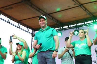 Rodrigo Kirchhofer sonríe con micrófono en mano, mientras dos mujeres aplauden y levantan las manos en un ambiente festivo.