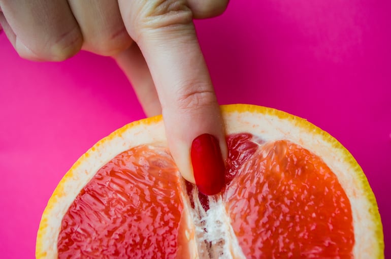 Dedos femeninos sobre un pomelo, concepto de vagina, clítoris, genitales.