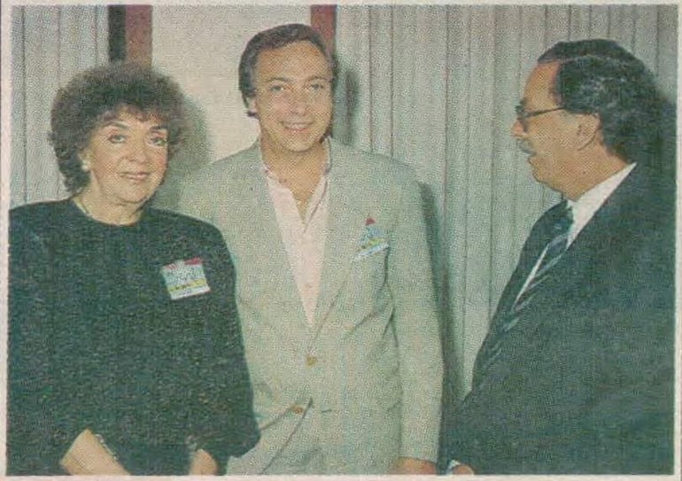 Nelly Prono con cabello rizado y camiseta negra, Luis Brandoni en camisa clara, y Richard Baddouh con traje y gafas, sonriendo.