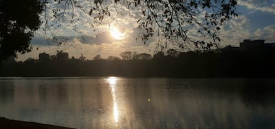 Un lago en primer plano con edificios al fondo bajo un cielo nublado, evocando tranquilidad y naturaleza.