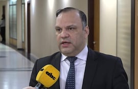 Mario Varela con traje oscuro y corbata de puntos, habla ante micrófono en pasillo iluminado en un ambiente formal.