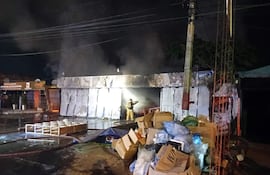 Bombero en equipo de protección lucha contra fuego en un edificio en llamas, mientras escombros y agua cubren el pavimento.