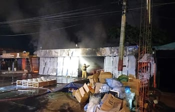 Bombero en equipo de protección lucha contra fuego en un edificio en llamas, mientras escombros y agua cubren el pavimento.