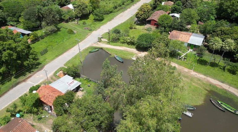 Perspectiva aérea de casas rodeadas de vegetación y agua del río Tebicuary, con varios barcos de madera en la orilla.