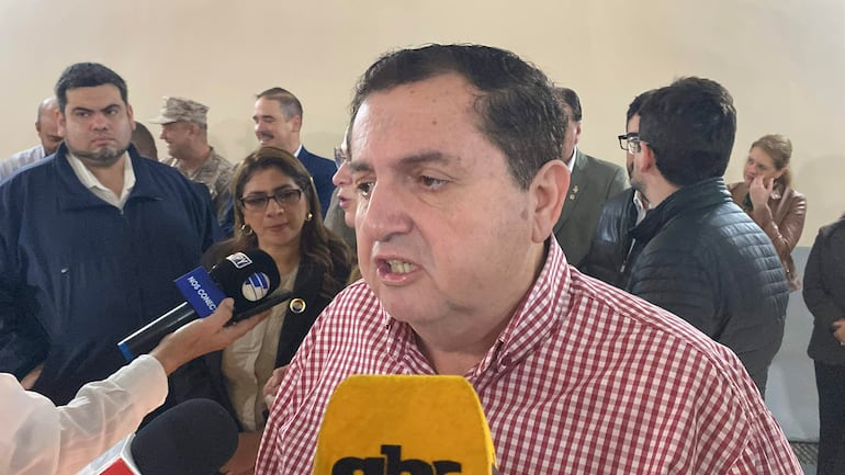 Arturo Urbieta en camisa de cuadros rojos responde a medios; María Teresa Barán con gafas en el fondo, ambiente formal.