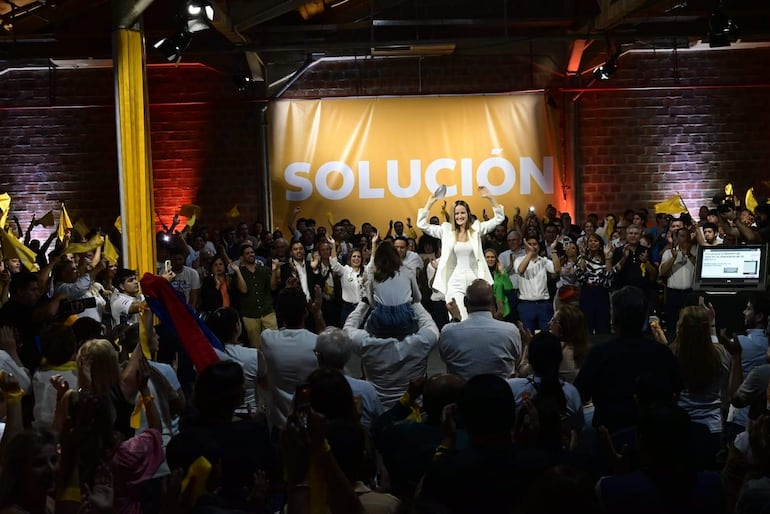 Soledad Núñez de pie levantando los brazos, rodeada de seguidores aplaudiendo y agitando pañuelos amarillos en un ambiente festivo.