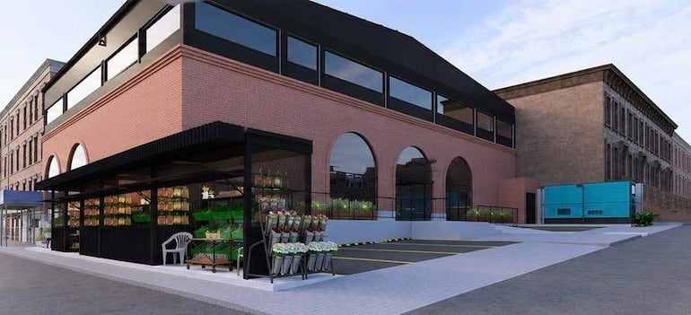 Edificio moderno de ladrillo y grandes ventanales, con tienda de productos frescos, en un ambiente urbano y pavimentado.