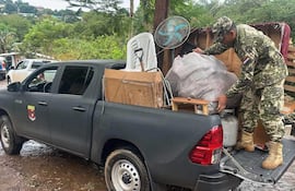 Hombres en uniforme militar cargan objetos en camioneta, rodeados de vegetación en un ambiente exterior.