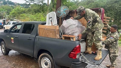 Hombres en uniforme militar cargan objetos en camioneta, rodeados de vegetación en un ambiente exterior.
