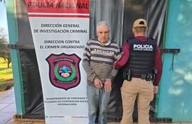 Sospechoso con camiseta de rayas esposado, junto a un agente de Policía Nacional en chaleco táctico, frente a pancarta institucional.