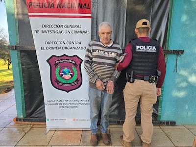 Sospechoso con camiseta de rayas esposado, junto a un agente de Policía Nacional en chaleco táctico, frente a pancarta institucional.