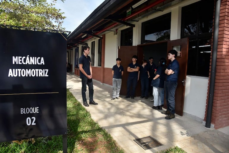 Grupo de jóvenes en bloque educativo, algunos con brazos cruzados, escuchando a un joven que presenta temas de mecánica automotriz.