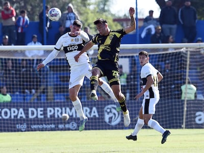 Junior Barreto (i), futbolista de Olimpia, disputa un balón aéreo en el partido frente a Recoleta FC por la fecha 22 del torneo Apertura 2025 de la Primera División de Paraguay en el estadio Luis Alfonso Giagni, en Villa Elisa, Paraguay.