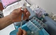 Persona concentrada en llenar jeringa con vacuna, en ambiente médico, rodeada de viales y jeringas.