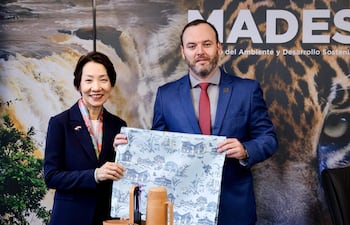 Rolando De Barros Barreto en traje oscuro y corbata roja, sonriente, junto a Grace Fu en chaqueta oscura y bufanda colorida, en un entorno de oficina.
